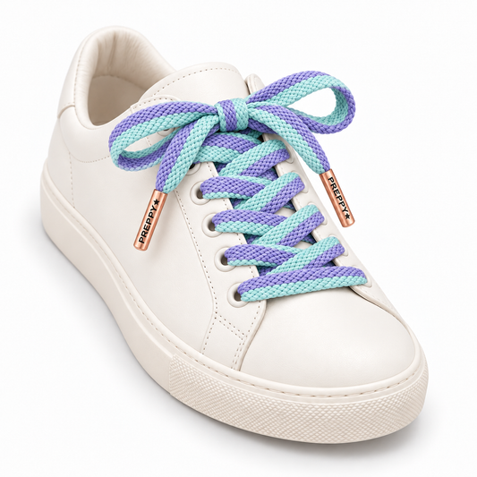A white leather low-top sneaker with chunky braided laces in pastel purple and mint green, featuring rose gold metal eyelets with 'PREYX' branding.