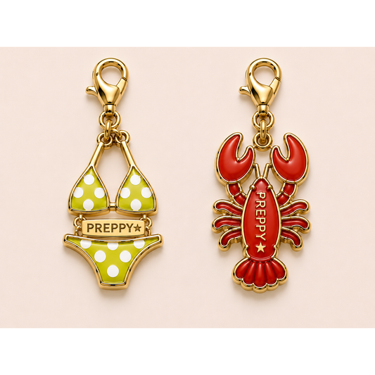 Two gold-tone charm pendants on a pale pink background: a bikini-shaped charm with green and white polka dots and a lobster charm in red with gold-tone trim and the word PREPPY.